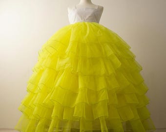 Pode incluir: Vestido formal exposto em um manequim. O vestido apresenta um corpete branco com decote quadrado e uma saia amarela volumosa e em camadas. A saia é feita de um tecido transparente, criando um efeito em camadas. Ideal para ocasiões especiais.
