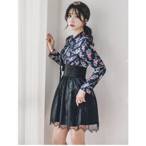May include: A navy blue floral print top with long sleeves and a black lace skirt. The dress has a wide black waist band and a decorative headpiece. The skirt has a scalloped lace hemline.