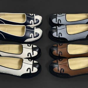 Puede incluir: Cuatro pares de zapatos sin cordones dispuestos en dos columnas. La columna izquierda muestra zapatos azul marino y blancos, mientras que la derecha muestra zapatos azul claro y marrones. Cada zapato tiene una punta redondeada con costuras negras.