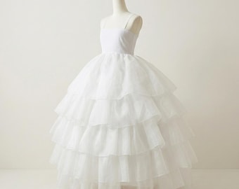Pode incluir: Um vestido de baile branco de tule em camadas, exibido em um manequim. O vestido apresenta um corpete justo com alças finas e uma saia volumosa composta por várias camadas de tecido fluido. O design é elegante.
