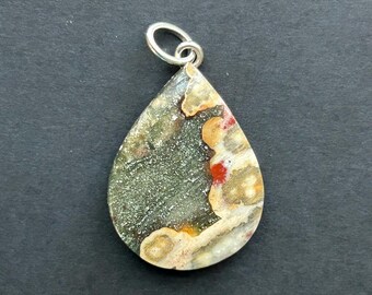 May include: A teardrop-shaped pendant featuring a polished stone with a mottled pattern of dark green, cream, tan, and bright red spots. The stone is set with a simple silver-toned metal bail at the top for attachment to a chain or cord.