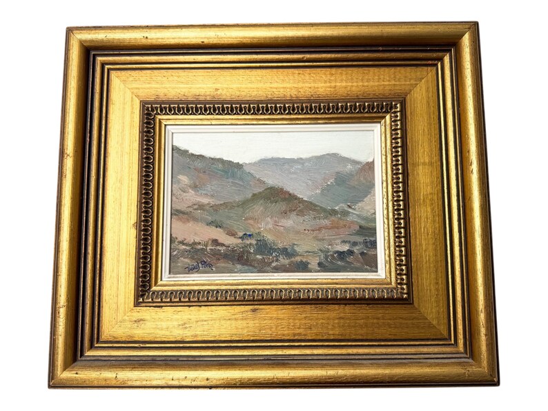 May include: A framed landscape painting with a gold-colored ornate frame. The painting depicts a mountain range in muted tones of green, brown, and gray. The frame has a double border with a detailed inner edge.