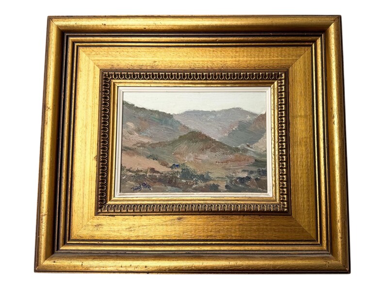 May include: A framed landscape painting featuring a mountain scene in muted tones of brown, green, and gray. The painting is set within a gold-colored, ornate frame, adding a touch of elegance to the artwork.