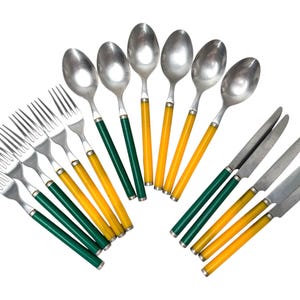 Può includere: Un set di posate composto da quattro forchette, cinque cucchiai e quattro coltelli. Ogni pezzo presenta una testa in metallo argentato e un manico a tinta unita giallo brillante o verde scuro, disposti a ventaglio su sfondo bianco.