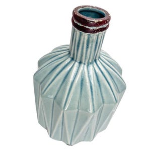 May include: A light blue ceramic vase with a geometric design. The vase has a textured surface and a narrow neck with a dark brown rim. The body of the vase has a faceted, angular shape.