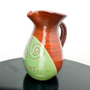 May include: A brown and green ceramic jug with a swirl design and the word "cases" on the side.