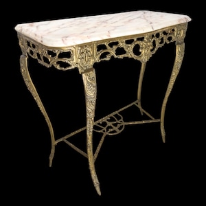 Op de afbeelding: Een rechthoekige consoletafel met een gepolijst wit marmeren blad met roze aders. Het onderstel is gemaakt van bewerkt, goudkleurig metaal met ingewikkeld krulwerk, gebogen poten en een decoratieve dwarsbalk die de vier poten met elkaar verbindt.