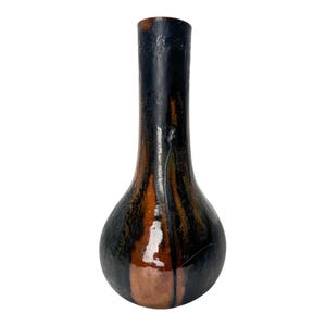 Puede incluir: Un jarrón de cerámica artesanal, alto, con base bulbosa y cuello estrecho. Presenta una llamativa paleta de colores negro, marrón y naranja, con vetas verticales y acabado brillante. Este jarrón decorativo es adecuado para la decoración del hogar.
