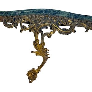 May include: An antique wall-mounted shelf with a green marble top and ornate gold-colored metalwork. The shelf features intricate floral and scroll designs, adding a touch of vintage elegance. The shelf is approximately 30 inches wide.