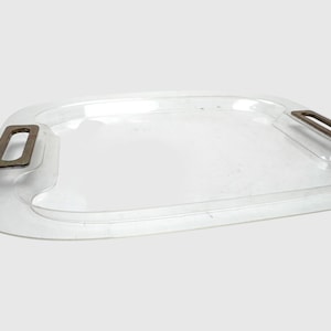 Könnte beinhalten: Ein rechteckiges Serviertablett aus klarem Acryl mit abgerundeten Ecken und zwei metallisch bronzefarbenen, rechteckigen Griffen an den Seiten. Das Tablett verfügt über eine glatte, transparente Oberfläche mit einem erhöhten Rand und Griffaussparungen.