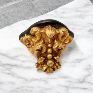 Puede incluir: Elemento arquitectónico decorativo dorado y ornamentado, con una parte superior marrón oscuro. El diseño presenta intrincados adornos y una serie de acentos esféricos. La pieza es probablemente de madera o un material similar.