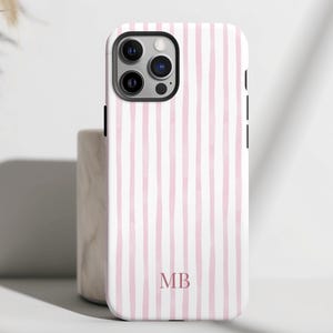 May include: White phone case with vertical pink stripes. The case has a camera cutout and black side buttons. The initials "MB" are printed in a matching pink color at the bottom of the case. The case is designed for a smartphone.