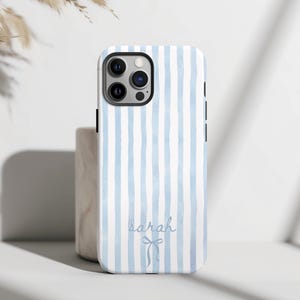 May include: A phone case with a light blue and white striped pattern. The case has the name "sarah" written in cursive with a bow graphic. The case is designed for a smartphone and has a camera cutout.