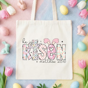 May include: Cream-colored tote bag with the words "He is Risen" in a colorful, patterned design, including bunny ears and a heart. The text "matthew 28:6" is also present. The bag is surrounded by Easter eggs, bunnies, and tulips.