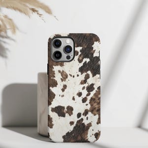 May include: A white and brown cowhide patterned phone case for an iPhone.