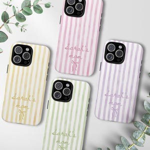 May include: Four phone cases with vertical striped patterns in yellow, pink, green, and purple. Each case has the text "Sarah's mom" in a cursive font, with a bow graphic. The cases are on a white surface with greenery.
