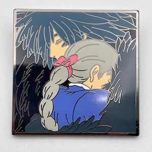 Puede incluir: Un pin de esmalte en blanco y negro que presenta una imagen estilizada de un hombre y una mujer abrazándose. El hombre tiene el pelo largo y negro y lleva una camisa azul oscuro. La mujer tiene el pelo largo y gris y lleva una camisa azul con un lazo rosa.