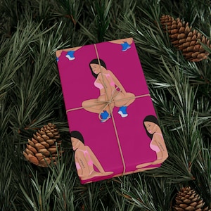 May include: A wrapped gift featuring a magenta background with a repeating illustration of a person in a pink bikini and blue shoes. The gift is tied with twine and set against a backdrop of pine needles and pine cones.
