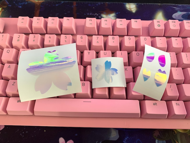 May include: Three sheets of white paper with holographic stickers of pink and blue flowers. The stickers are iridescent and have a rainbow effect.