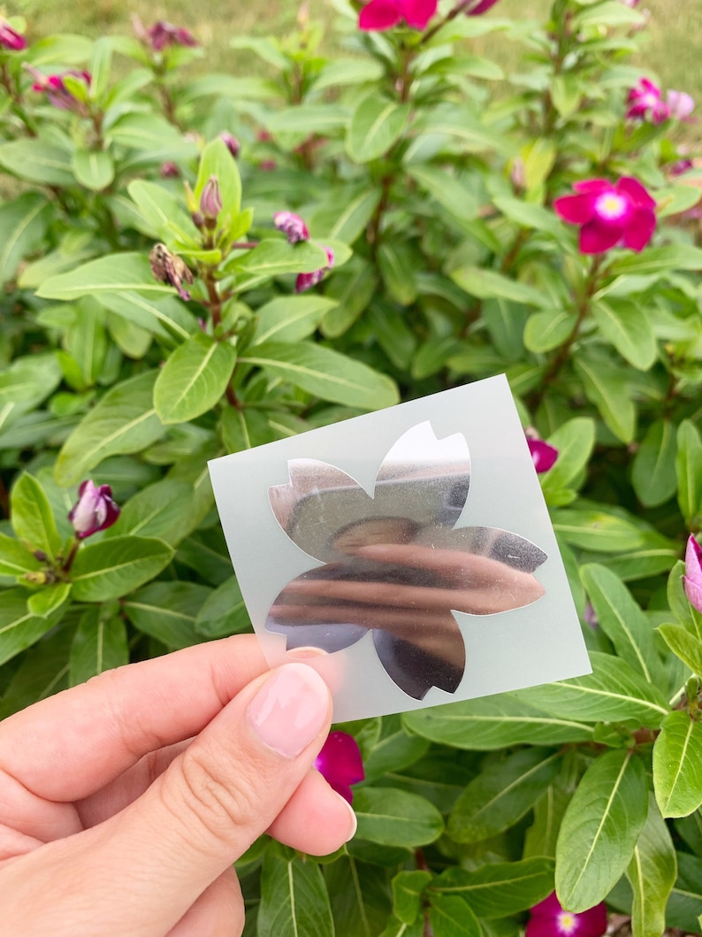 May include: A silver sticker with a five-pointed star shape, resembling a flower. The sticker is on a clear sheet of paper.