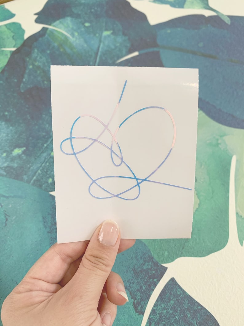 Op de afbeelding: Een witte sticker met een hartvormig ontwerp in blauw, roze en paars. Het hart is gemaakt van &eacute;&eacute;n doorlopende lijn.