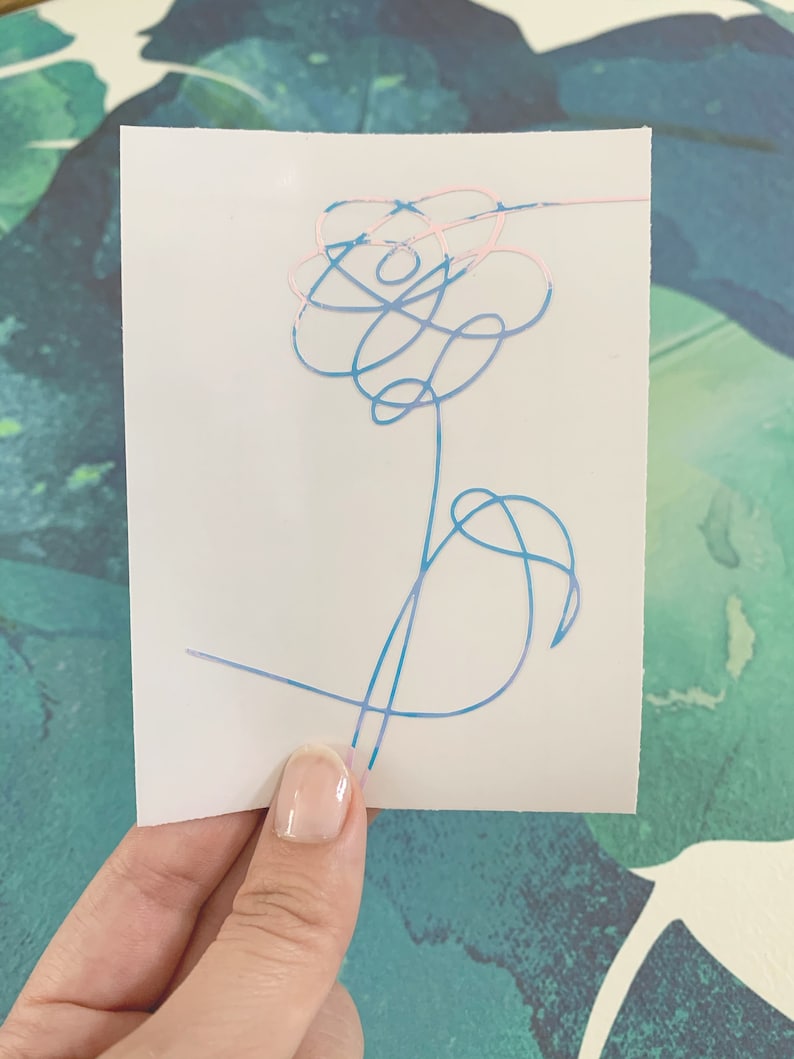 Op de afbeelding: Een sticker met een blauw en roze bloemetjesontwerp. De bloem is getekend in een eenvoudige, abstracte stijl.