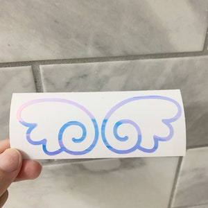 May include: A sticker with a pair of iridescent blue and pink angel wings. The wings have a swirl design.