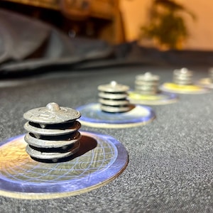 May include: A close-up of a board game with several stacks of silver-colored game pieces on circular game boards. The game pieces are stacked on top of each other. The game boards have a blue and yellow design.