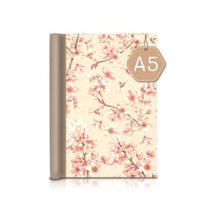 Könnte beinhalten: A5-Notizbuch mit beigefarbenem Einband und floralem Design aus rosa Kirschblüten. Der Buchrücken ist einfarbig beige. Ein braunes Etikett mit dem Text "A5" hängt oben.