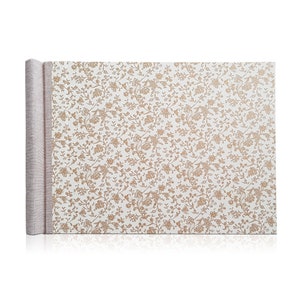 May include: A white photo album with a brown floral pattern on the cover. The album has a linen spine and is closed.
