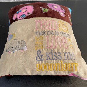 May include: A brown and beige pillow with embroidered text that reads "read me a story then tuck me in tight tell me you love me & kiss me goodnight". The pillow features a pink elephant and a blue elephant.