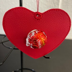 以下が含まれることがあります： 赤いフェルトのハート型のオーナメントで、中にリンツのチョコレートトリュフが入っています。オーナメントの上部には、吊り下げ用の小さなループが付いています。