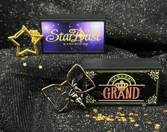 May include: Two black boxes with neon signs. The top box has the text "Star Dust Kamurocho" in a white font. The bottom box has the text "Cabaret Grand" in a red font with a gold crown above the text.