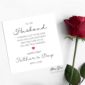 May include: A white card with black text that reads "To My Husband It Means A Lot To Me How Much You Love Our Family And Take Care Of Us. You Are Truly Amazing Happy First Father's Day With Love" with a red heart symbol. The card has a black and white logo that reads "Happy Days Stationery".