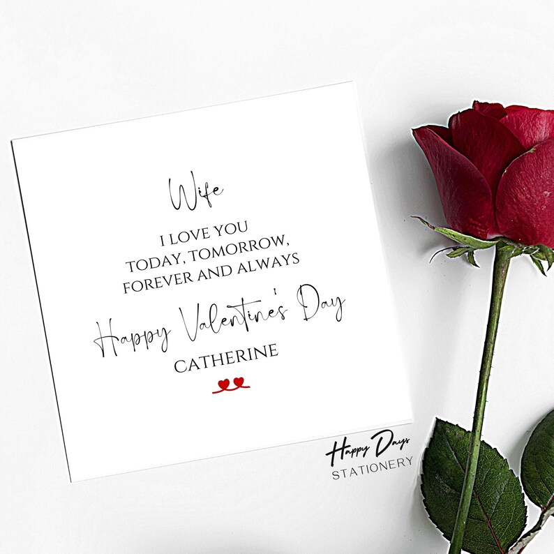 May include: A white card with black text that reads "Wife I love you today, tomorrow, forever and always Happy Valentine's Day Catherine" with two red hearts. The card is on a white background with a red rose.