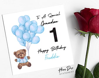 May include: A white card with a blue teddy bear holding blue balloons. The card says "To A Special Grandson 1 Happy Birthday Freddie" and "Happy Days Stationery".