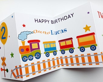 May include: A colourful birthday card with a train theme. The card features a train with a red engine, blue, red, and orange carriages, and a yellow star. The card says "Happy Birthday" and "Choo choo Lucas" and "Two".
