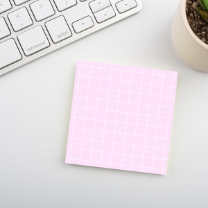 Peut inclure: Un bloc-notes adhésif rose avec un motif quadrillé blanc sur une surface blanche. Le bloc-notes est vierge et prêt à être écrit.