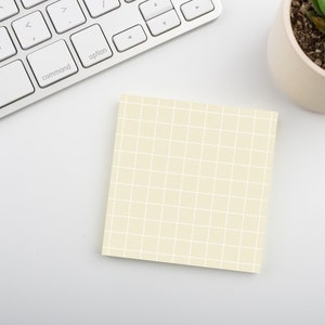 May include: A white keyboard with a light beige sticky note on a white surface. The sticky note has a grid pattern.