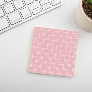 May include: A pink gridded sticky note on a white surface.