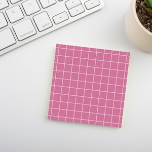 May include: A square, pink sticky note with a white grid pattern. The note is on a white surface next to a computer keyboard and a small potted succulent.