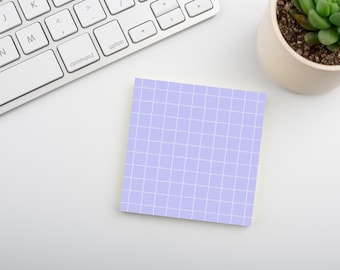 May include: A square sticky note featuring a light purple background with a white grid pattern. The paper is positioned on a flat surface next to a white computer keyboard and a small potted succulent plant, providing a clear view of the grid design.