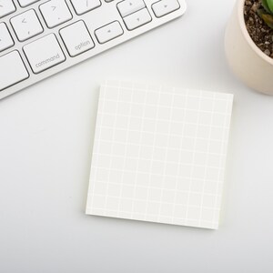 May include: A white keyboard with a white sticky note with a grid pattern on a white surface. A small potted succulent plant is in the upper right corner of the image.