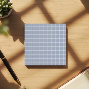 Puede incluir: Un bloc de notas cuadrado azul claro con un patrón de cuadrícula blanco. Una pluma estilográfica negra y dorada, una pequeña planta suculenta en maceta y un cuaderno abierto están sobre un escritorio de madera. La escena está iluminada por luz natural, proyectando sombras.