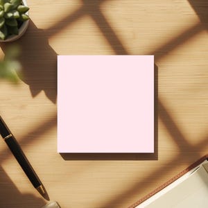 Puede incluir: Vista aérea de un escritorio de madera con una nota adhesiva cuadrada rosa claro. También hay una pluma estilográfica negra y dorada, una pequeña suculenta en una maceta blanca y un cuaderno abierto. La escena está iluminada por la luz del sol.