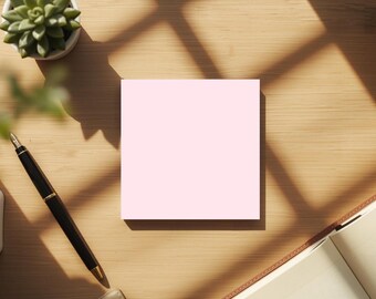 May include: Overhead shot of a wooden desk with a light pink square sticky note. A black and gold fountain pen, a small succulent in a white pot, and an open notebook are also on the desk. The scene is lit by sunlight.