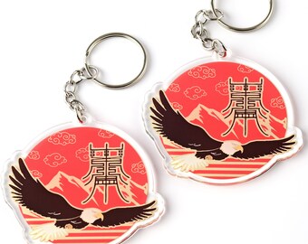 May include: Two red and white acrylic keychains with a gold eagle design and Chinese characters. The keychains feature a red background with white clouds and mountains, and a gold eagle flying over a striped pattern.