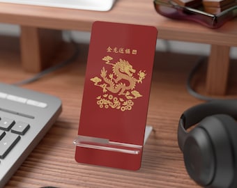 May include: A red phone stand with gold Chinese characters and a gold dragon design. The stand is on a wooden desk with a keyboard, headphones, and a computer monitor in the background.