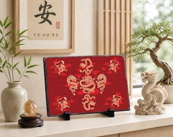 May include: A rectangular red slate plaque featuring gold dragon designs. The dragons are surrounded by red clouds. The plaque is displayed on a black stand. A framed artwork with Chinese characters is in the background.