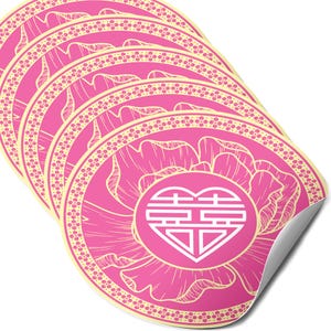 May include: A stack of pink, round stickers with a floral design and a heart-shaped symbol in the center. The stickers have a cream-colored border with a dotted pattern. The heart symbol is white.